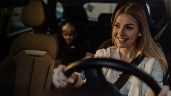 A Woman driving a car with a child in the back seat; faces blurred for privacy.