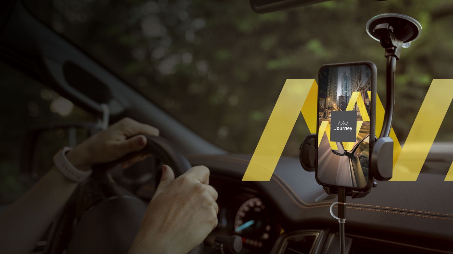Close-up of hands on a car steering wheel with a mounted cellphone on the windshield displaying the Aviva Journey telematics app.