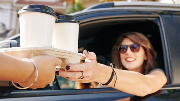 Woman smiling and reaching for a coffee in drive through