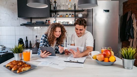 Un couple assis près de la table de la cuisine couverte de papiers et de plans. 