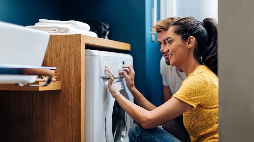 Couple using a front load washing machine to wash laundry.