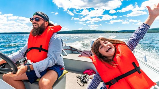 Père et fille portant des gilets de sauvetage sur un petit bateau profitant d'une journée sur l'eau.  
