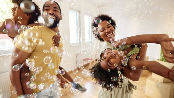 Une famille enjouée qui danse avec des bulles dans le salon après avoir emménagé dans une nouvelle maison.  