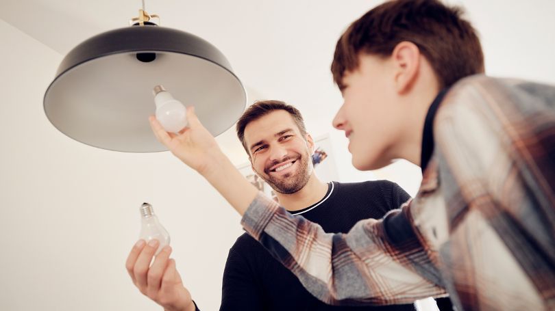 Un père et son fils remplacent une ampoule traditionnelle par une ampoule à DEL à faible consommation énergétique.