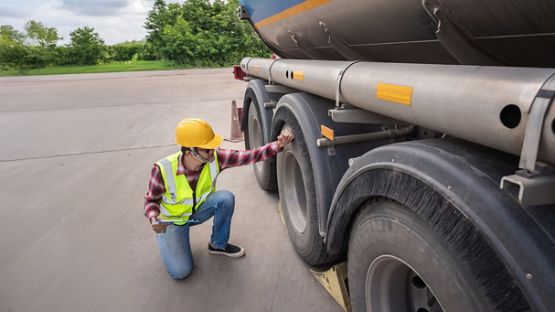 Un homme à l'extérieur vêtu d'un gilet de sécurité accroupi pour inspecter les écrous de roue d'un camion de transport