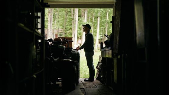 A man standing in the doorway of his garage, with a well-maintained ATV parked inside.