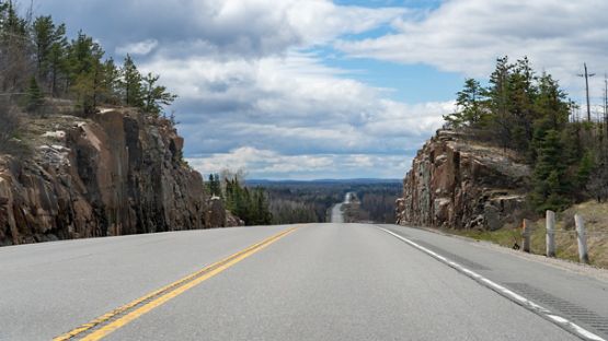 A road with the Canadian Shield terrain sloping up from the side