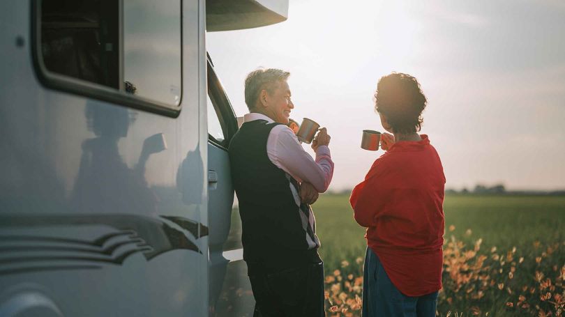 Un couple de personnes âgées profitant d'une pause-café devant leur autocaravane.