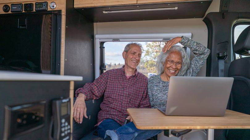 A senior couple using a laptop computer while relaxing in their customized camper van