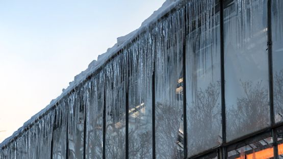 Accumulation de neige sur le toit d’un bâtiment commercial avec de grands glaçons suspendus à l'extérieur des murs de verre.