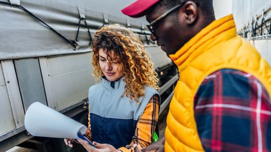 A woman and a man review a vehicle safety checklist while outside next to a transport truck