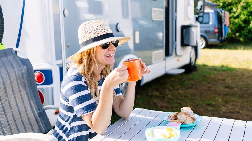 A woman sitting next to a RV enjoying breakfast with a peace of mind