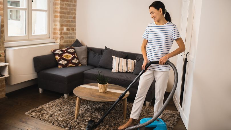 A woman vacuuming a rug in her condo living room.