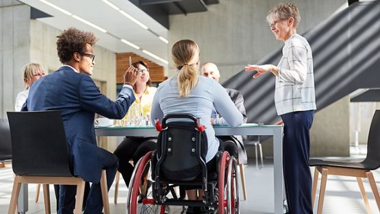 Une femme anime une réunion et s’adresse aux employés assis autour d’une grande table. 