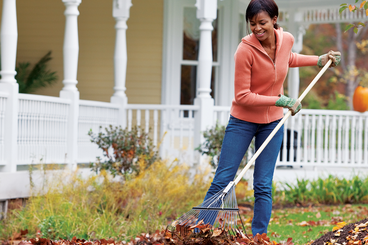 Une femme ramasse les feuilles mortes devant sa maison.