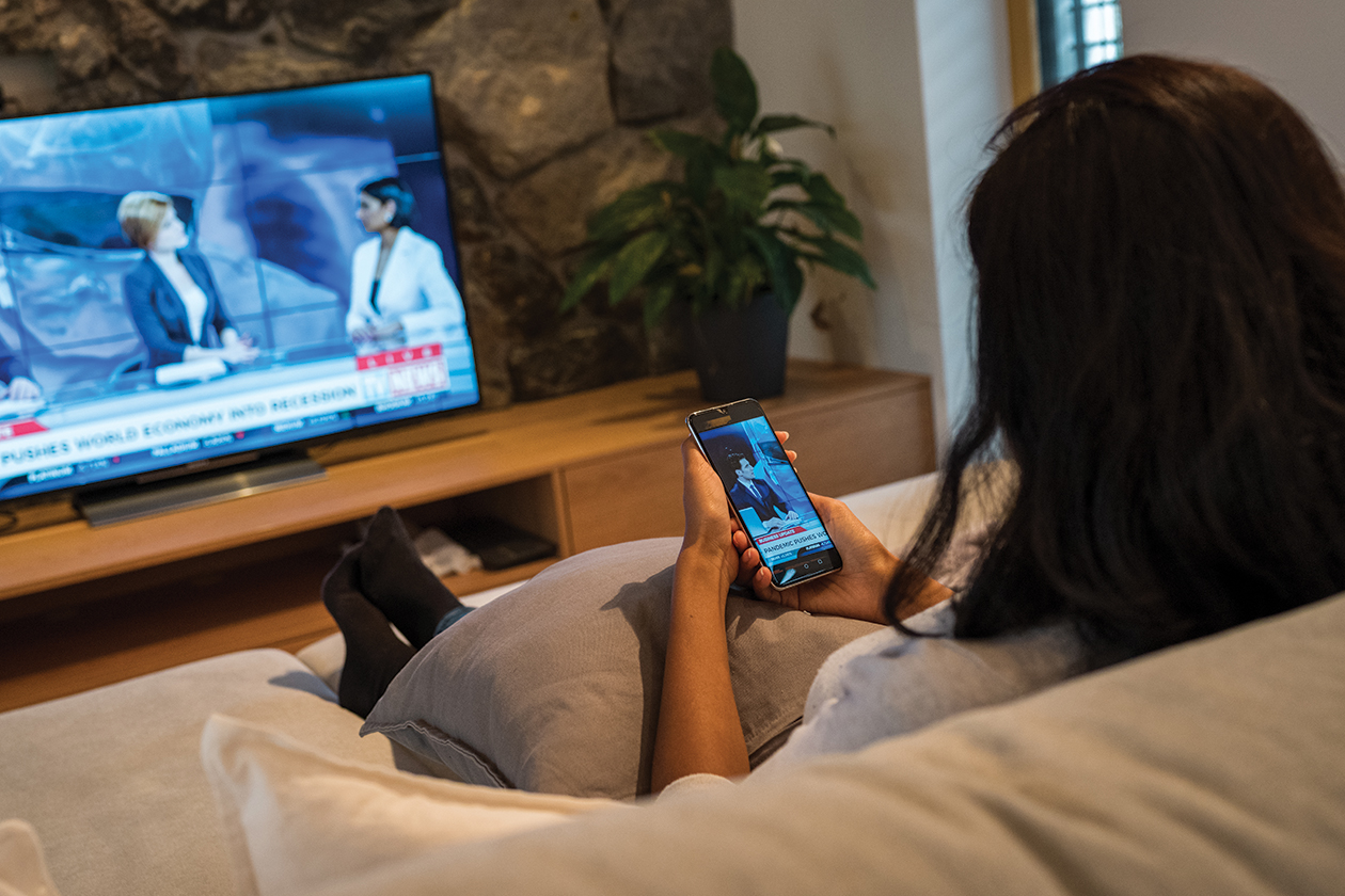 Une femme regarde le bulletin d’information local à la télévision et consulte les alertes d’urgence sur son téléphone.